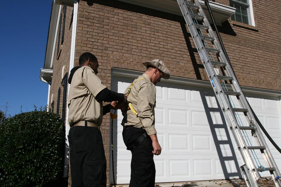 A technician fits a safety harness on his partner as they prepare to climb a ladder to a client’s roof.