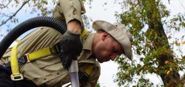 A franchisee in an outback-style hat uses a ThunderVac™ against a backdrop of leafy trees.