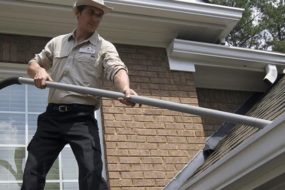 An Outback GutterVac technician vacuums leaves from a rooftop gutter.
